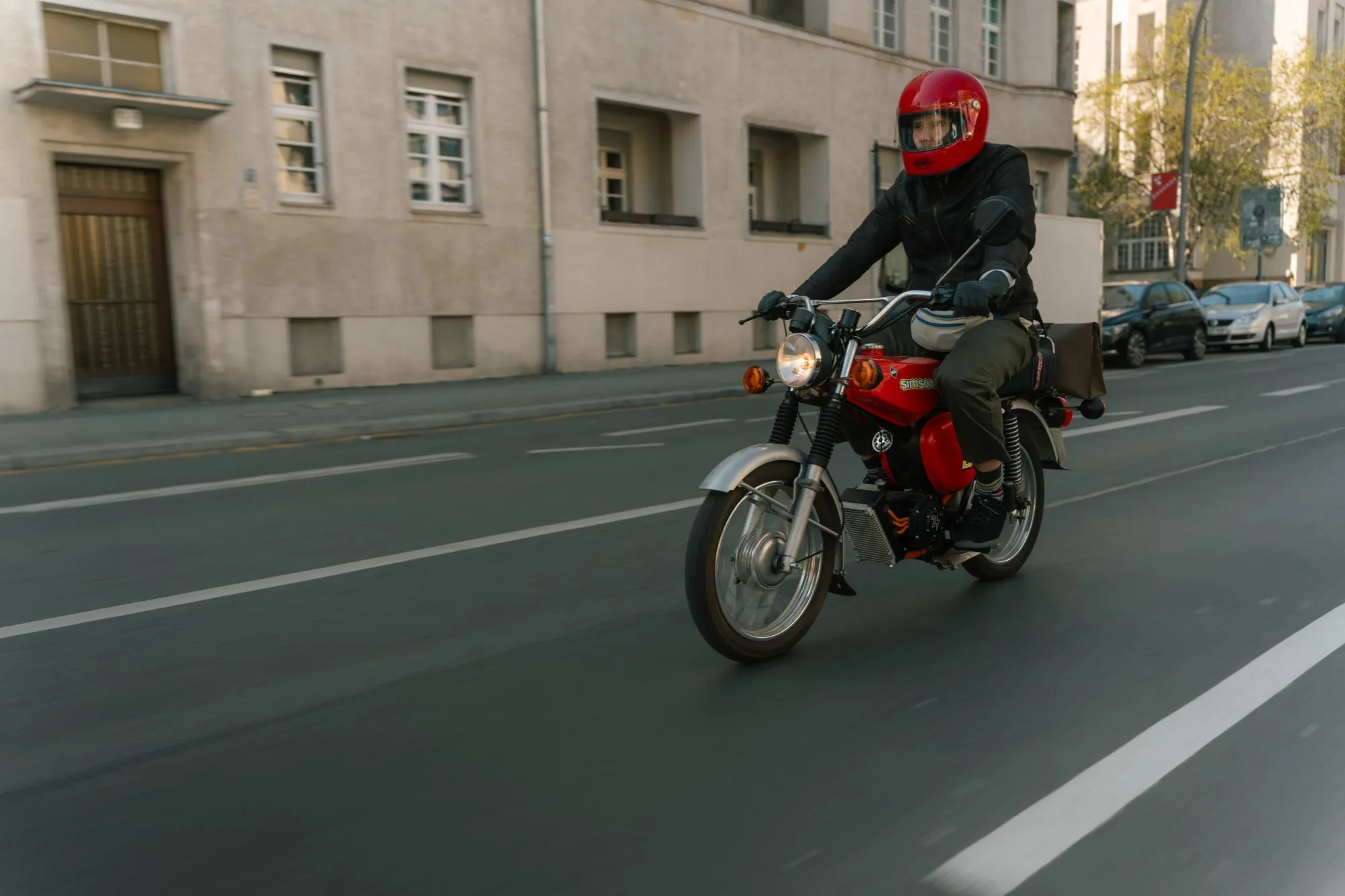 fahrer mit rotem helm auf einer roten simson, mitzieher auf berliner straße