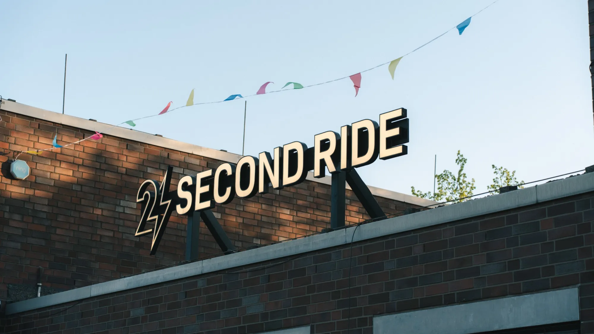 leuchtschrift „second ride“ auf dem backsteingebäude mit bunten wimpeln