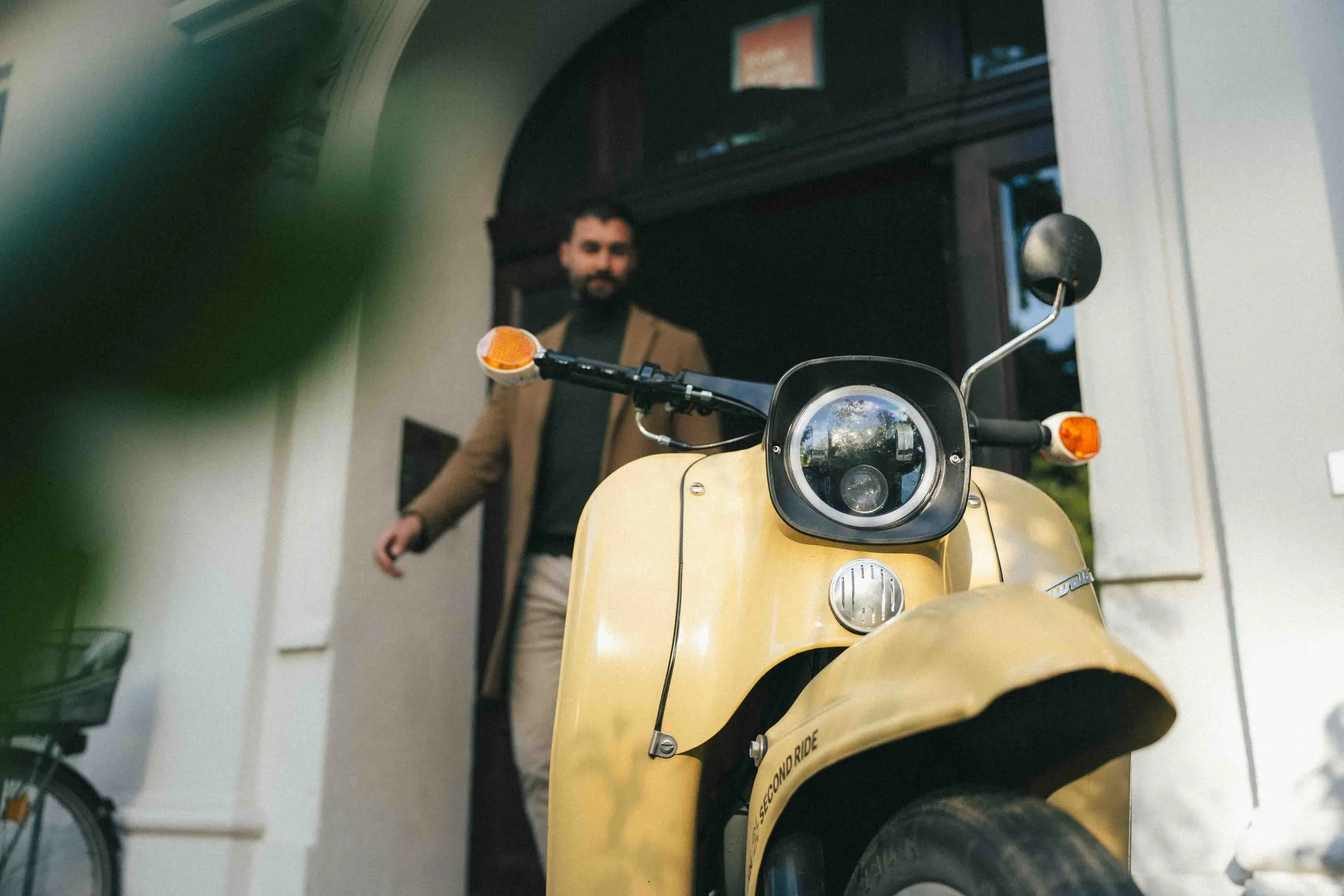 nahaufnahme des scheinwerfers am gelben moped, im hintergrund ein mann, der aus einem torbogen tritt