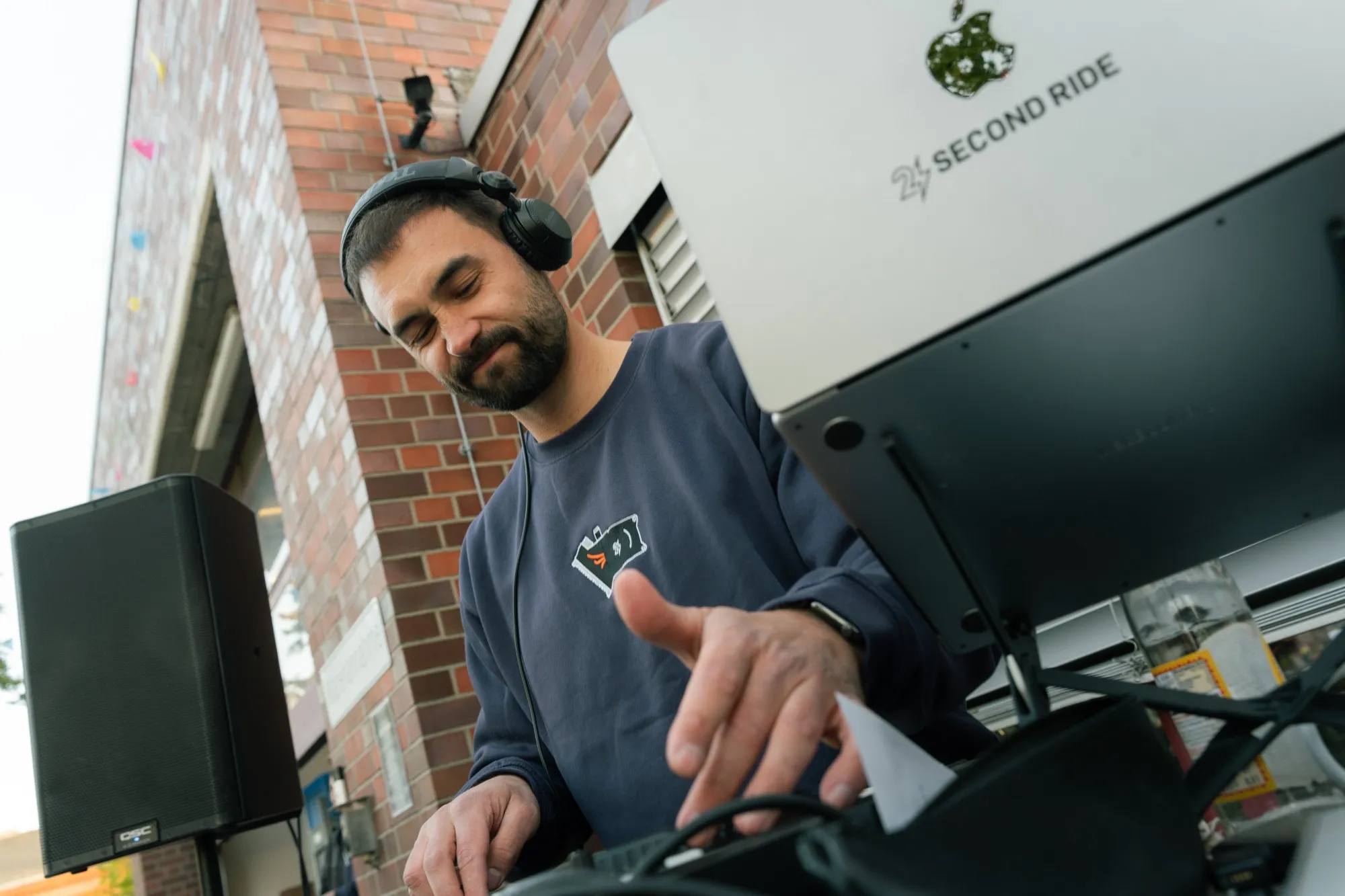dj mit kopfhörern am pult, laptop mit second-ride-logo im vordergrund