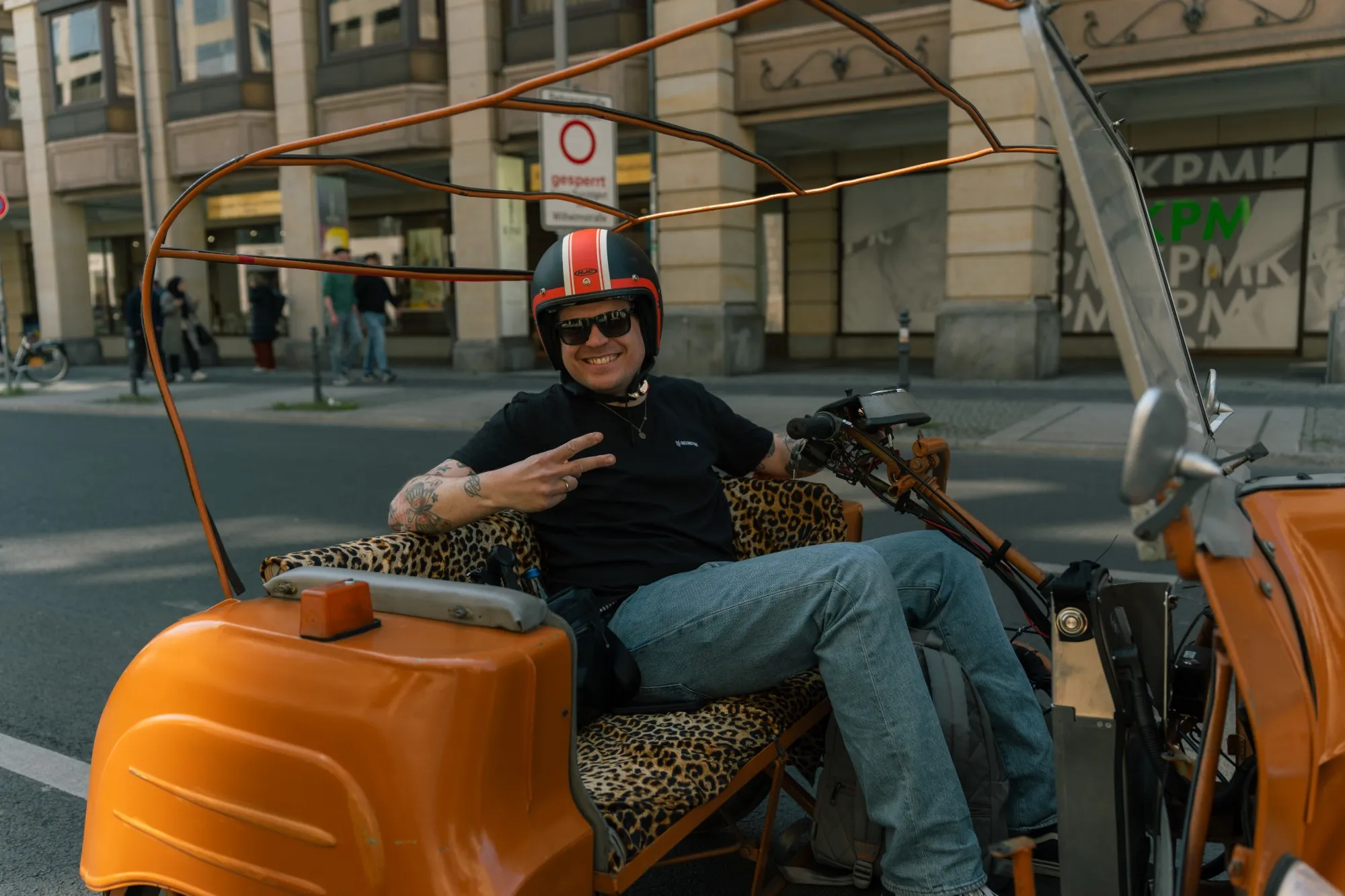 lachender teilnehmer mit peace-zeichen in einem orangen simson-duo mit leopardenbezug