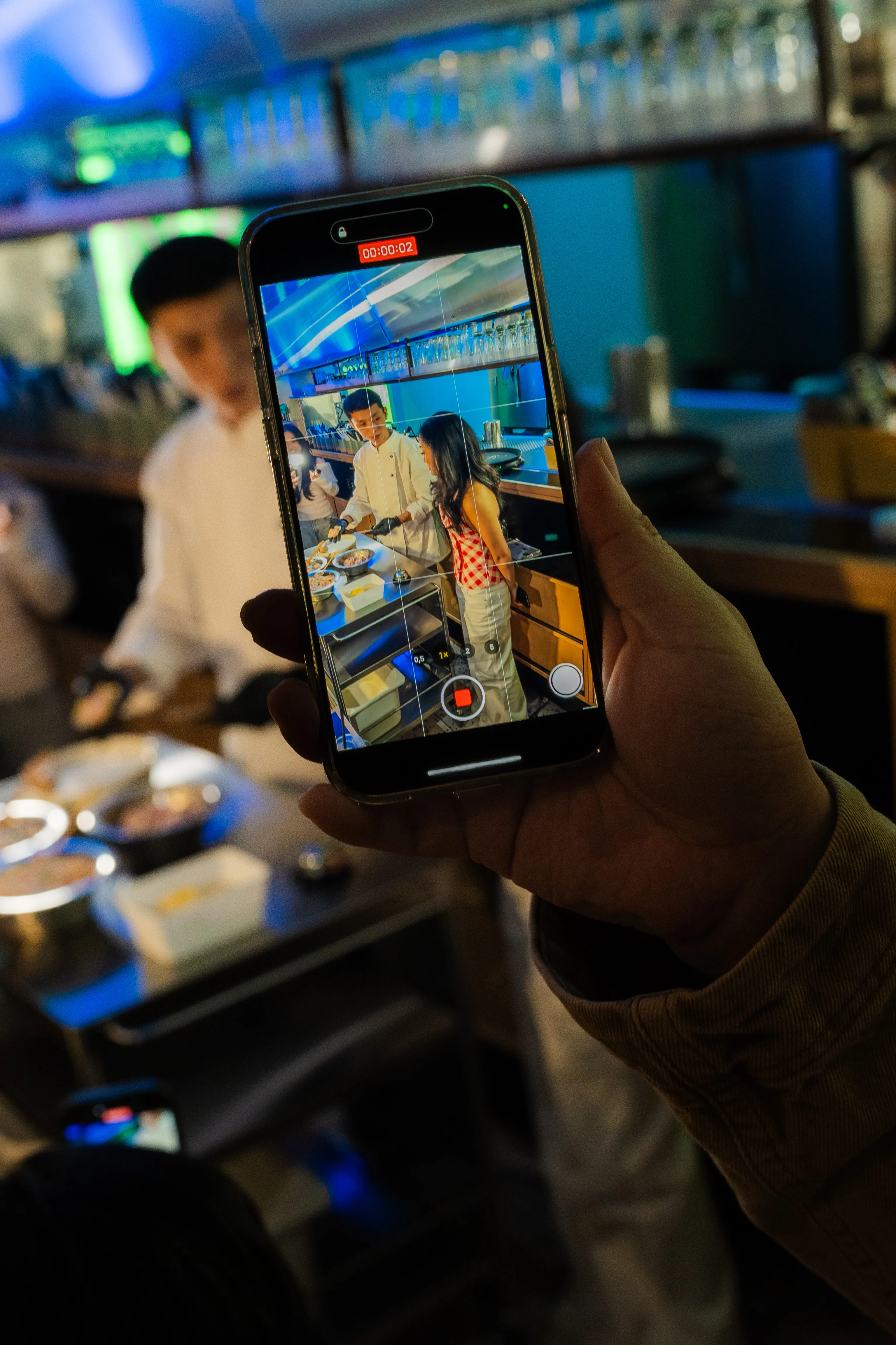 smartphone-bildschirm filmt koch und gästin beim kochen hinter der theke