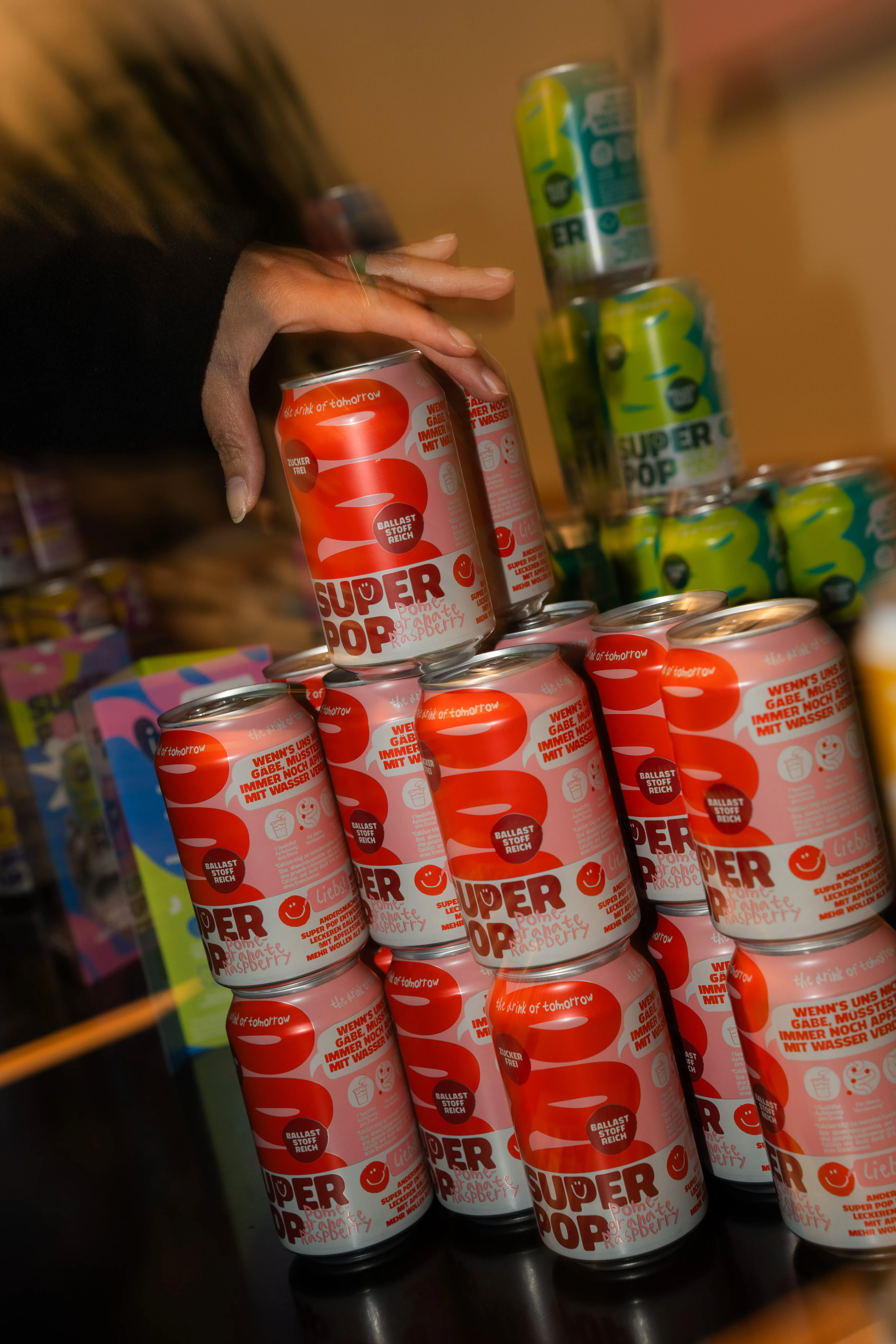 gestapelte „super pop"-getränkedosen als pyramide, hand setzt eine dose obenauf